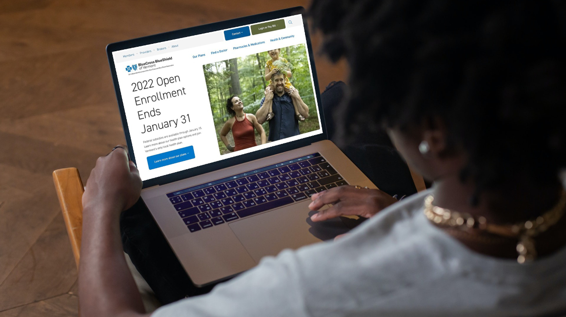 A woman sits in a chair reviewing health insurance plans on her laptop