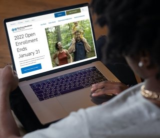 A woman sits in a chair reviewing health insurance plans on her laptop