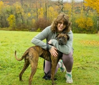 A woman kneeling on the ground hugging her dog