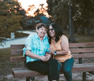 An older mother and her daughter sit together on a bench in the park