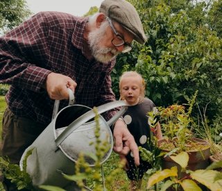 An older man waters plants with his granddaughter 