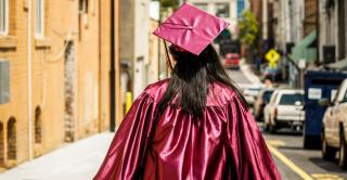 A woman walks down a deserted street wearing a cap and gown
