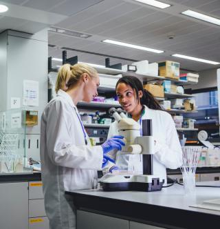 Two students talking in a lab next to a microscope