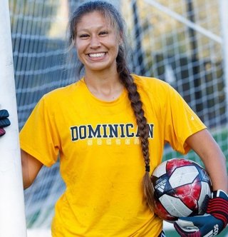 A woman holding a soccer ball wearing a Dominican University shirt