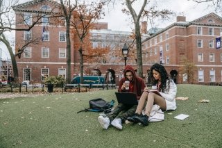 Two students sit on the grass studying