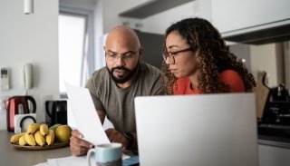 A couple sit together in a kitchen discussing health insurance plan options