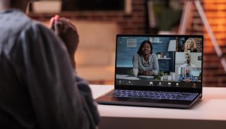 A woman sits at a desk watching a webinar