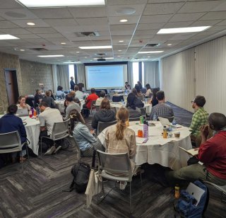 A group of Bootcamp attendees seated at round tables watching a presentation at the front of the room
