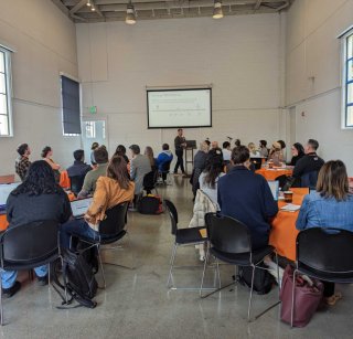 A group of Bootcamp attendees seated at round tables watching a presentation at the front of the room