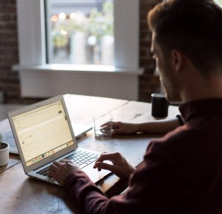 A man sits at a bench typing on a laptop