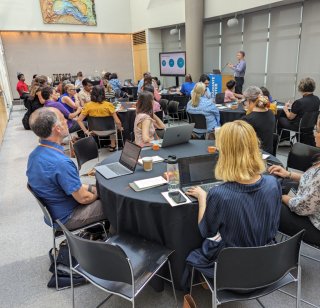A group of Bootcamp attendees seated at round tables watching a presentation at the front of the room