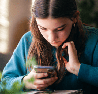 Girl on her phone in front of a laptop